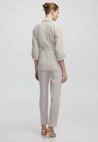 Beiger taillierter Blazer mit 3/4-Ärmeln, taillierter Detail, kombiniert mit passenden geraden Hosen und Riemchen-High Heels.