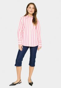 Long-sleeve, button-up shirt with pink and white vertical stripes, featuring a chest pocket and a classic collar, paired with dark denim capris.