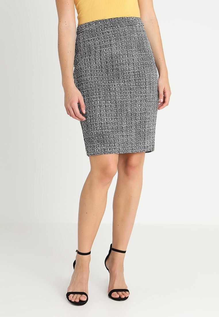 Schwarzer und weißer Tweed-Bleistiftrock mit einer taillierten Silhouette, strukturiertem Stoff und einer Länge bis zur Mitte des Oberschenkels, kombiniert mit schwarzen Riemchenabsätzen.