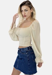 Beige langærmet top med firkantet U-hals og rynkede detaljer, parret med en blå denim mini-nederdel med en frynset kant og frontlommer.