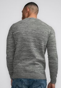 Gray knit sweater with a textured pattern, round neckline, and ribbed cuffs and hem. Worn with blue denim jeans.
