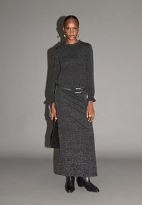 Vestito nero in maglia con maniche lunghe, aderente al busto e con gonna lunga e fluente. Presenta una vita con cintura e una texture leggermente scintillante.