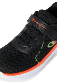 Scarpa da ginnastica nera con texture in rete, accenti arancioni, cuciture verdi e una fascetta in Velcro con il marchio "Champion".