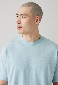 Lyseblå kortærmet t-shirt lavet af et tekstureret stof. Har en rund halsudskæring og et diskret broderet Levi's-logo på forsiden.