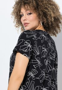 Camisa negra con patrones florares y lazos dibujados a línea en blanco, de mangas cortas y corte relajado. Textura suave y tela ligeramente elástica.