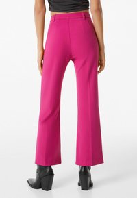 Fuksjowe spodnie z szerokimi nogawkami o gładkiej teksturze, dopasowane do sylwetki, z szlufkami na pasek, w zestawie z czarnymi botkami na obcasie.