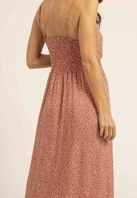 Robe maxi rouge à fleurs avec un dos froncé, des bretelles fines réglables et une coupe décontractée. Motif de petites feuilles blanches sur l'ensemble du tissu.