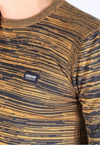 Sweter z długim rękawem z prążkowanym wzorem w złoto i granatowo, teksturowanym dekoltem oraz czarną metką z białym napisem.