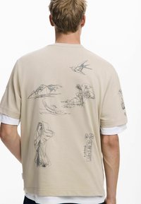 Beige short-sleeve shirt with back graphic design featuring embroidered mountains, birds, flowers, and figures in contrasting dark threads.