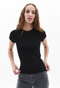 Černé ribbed tričko s krátkým rukávem, se přiléhavým designem a kulatým výstřihem, spárované se šedými kalhotami s vysokým pasem. Hladká textura.