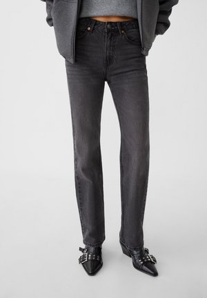 Person wearing high-waisted faded black straight-leg jeans, cropped gray sweater, gray jacket, and black pointed shoes with buckles.