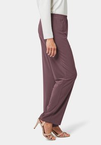 Auberginekleurige, lichte broek met een elastische tailleband, ontworpen voor comfort. Gepaarde met beige sandalen met riempjes.