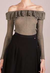 Schulterfreies, tailliertes Oberteil in Grau mit gerippter Textur und Rüschensaum, kombiniert mit einem schwarzen, ausgestellt geschnittenen Rock mit glatter Oberfläche.