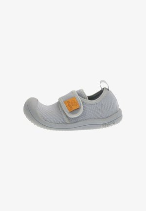 Scarpa da bambino in tessuto grigio chiaro con punta in gomma, chiusura a strappo e etichetta arancione con logo sul lato.