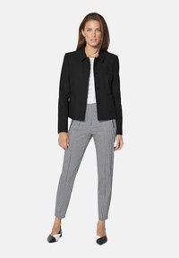 Zwarte op maat gemaakte blazer met een puntige kraag, voor knopen en twee zakken. Gecombineerd met zwart-witte hondenstooth broek en bicolor schoenen.