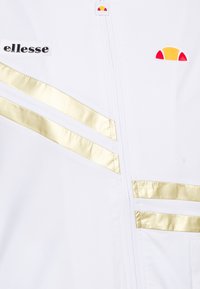 Weißer Jacke mit goldenen Satinstreifen, Reißverschluss und Markenlogo "ellesse". Mit buntem Logo über dem Reißverschluss. Glatte Textur.