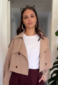 Beige kort jacka med dubbelknappar över en vit t-shirt, kombinerad med vinröda byxor med hög midja. Långt, löst brunt hår.