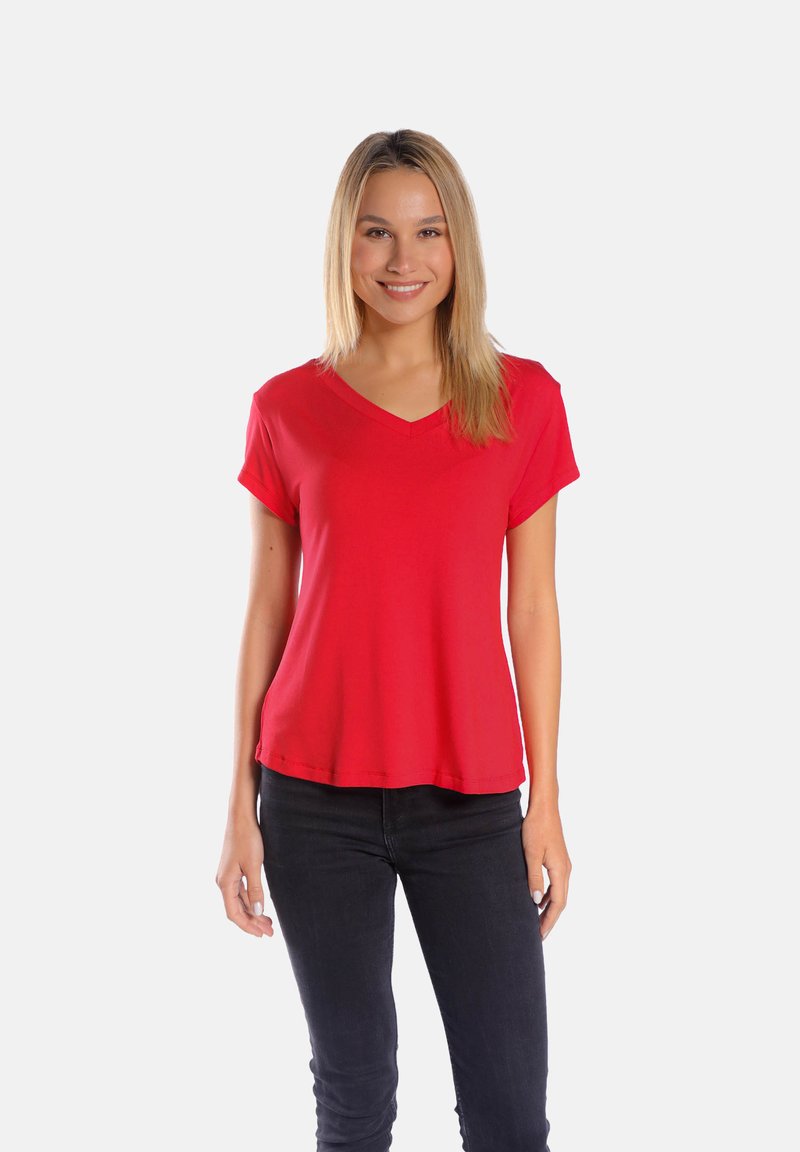 Czerwona, krótka koszulka z dekoltem w serek, wykonana z miękkiego, lekkiego materiału, o luźnym kroju i prostym wykończeniu. Noszona z czarnymi dżinsami.