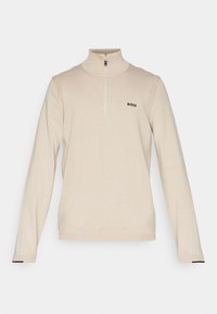 Pull-over beige à col zippé en tissu doux, avec manches longues, texture côtelée et petit logo noir sur la poitrine.
