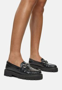 Black leather loafers with a crocodile texture, rounded toe, and silver hardware detail. Thick black rubber sole for added height and grip.