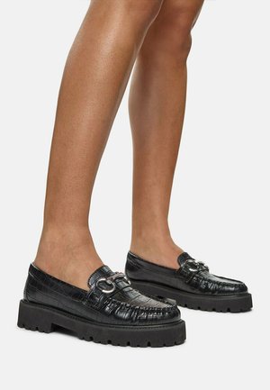 Black leather loafers with a crocodile texture, rounded toe, and silver hardware detail. Thick black rubber sole for added height and grip.