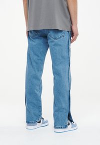 Vaqueros de mezclilla en azul claro, con botones a presión a lo largo del costado, diseño de pierna recta y una textura ligeramente deslavada.