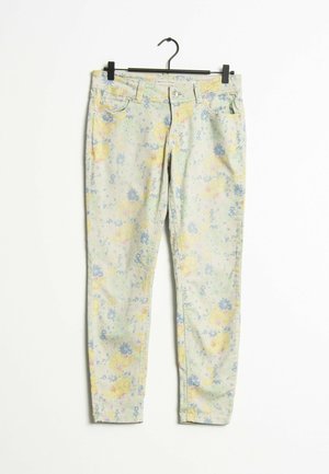 Slim-fit lichte denim broek met pastelgele en blauwe bloemenprint, met knoop- en ritsluiting, hangend aan een zwarte hanger.