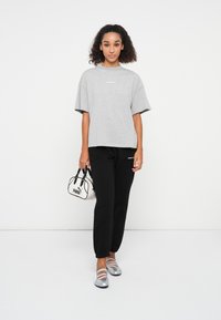 Gray oversized t-shirt with short sleeves, black sweatpants, silver flats with straps, and a small black and white handbag.