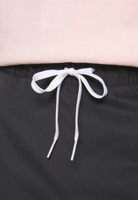 Pantaloni corti neri con cintura elasticizzata e laccio, caratterizzati da una corda intrecciata bianca. Il tessuto appare liscio, con una leggera lucentezza.