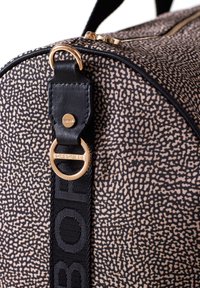 Borsa da palestra a motivo nero e beige con un anello in metallo dorato. Presenta una superficie testurizzata, una fascia con logo audace e una chiusura con zip.