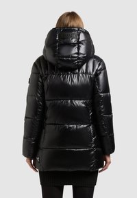 Svart puffjacka med glänsande yta, utrustad med huva, quiltad textur och logotypdetalj på baksidan. Räfflad fåll och långa ärmar.