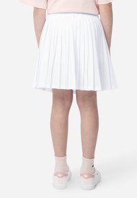 Λευκή πλισέ φούστα με ελαστική μέση. Φορεμένη με λευκά αθλητικά παπούτσια με ροζ λεπτομέρειες και ανοιχτόχρωμες κάλτσες αστραγάλου.