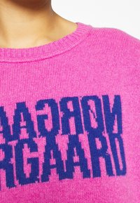 Pull rose tricoté avec un col rond, arborant en évidence un lettrage bleu bloc, "NORGAARD", affiché sur le devant.