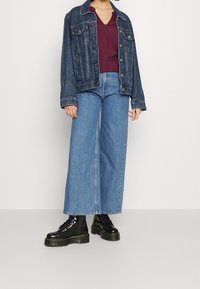 Giacca di denim blu scuro, abbinata a un top amaranto a scollo a V e a jeans a gamba larga blu chiaro. Stivali neri con zeppa e lacci.