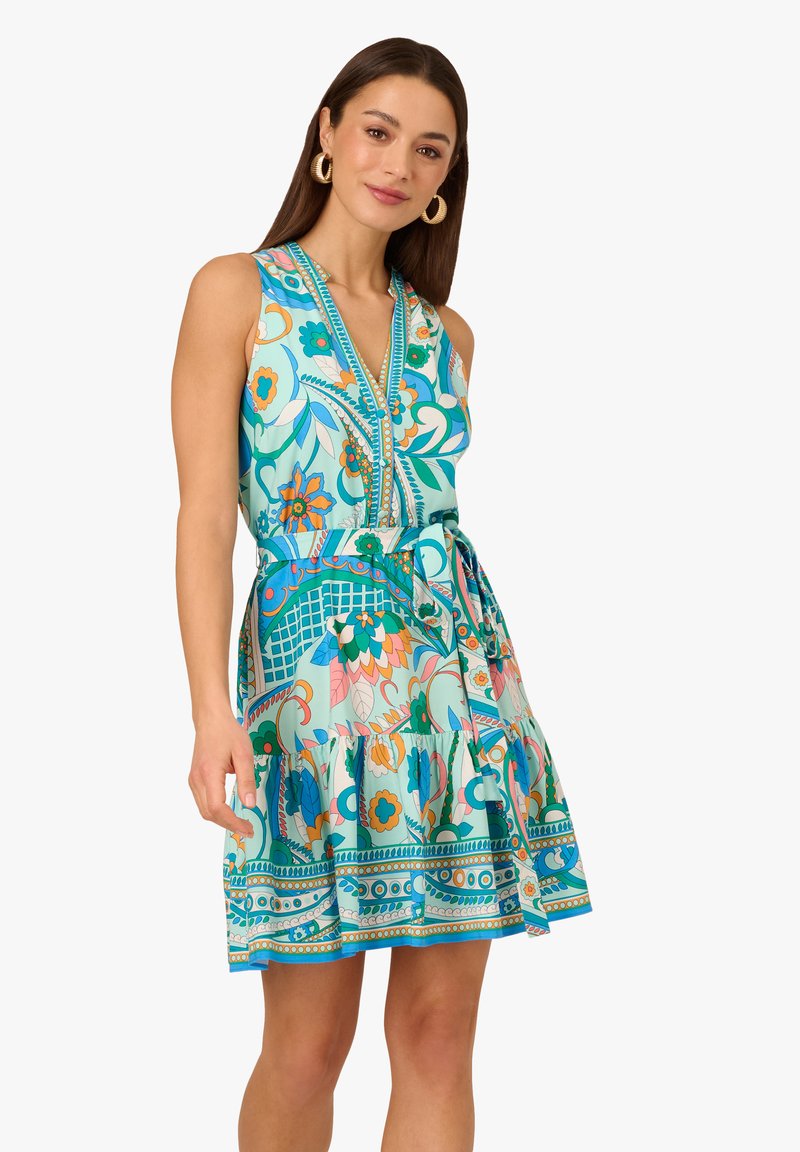Abito senza maniche, scollato a V in teal con motivi floreali e geometrici. Presenta una vita cinchata e un orlo a balze a strati. Tessuto leggero.