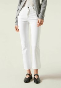 Jeans blancos de pernera recta con cintura alta, que cuentan con un cierre de botón y bolsillos frontales. Combinados con zapatos Mary Jane negros.