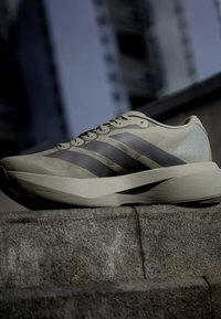 Μπεζ και μαύρο παπούτσι για τρέξιμο Adidas τοποθετημένο σε πέτρινα σκαλοπάτια με θολό φόντο κτιρίου σε χαμηλό φωτισμό.