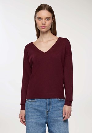 Maglione bordeaux a collo a V con maniche lunghe, tessuto morbido e polsini a costine, abbinato a jeans di denim blu chiaro. Design semplice e casual.