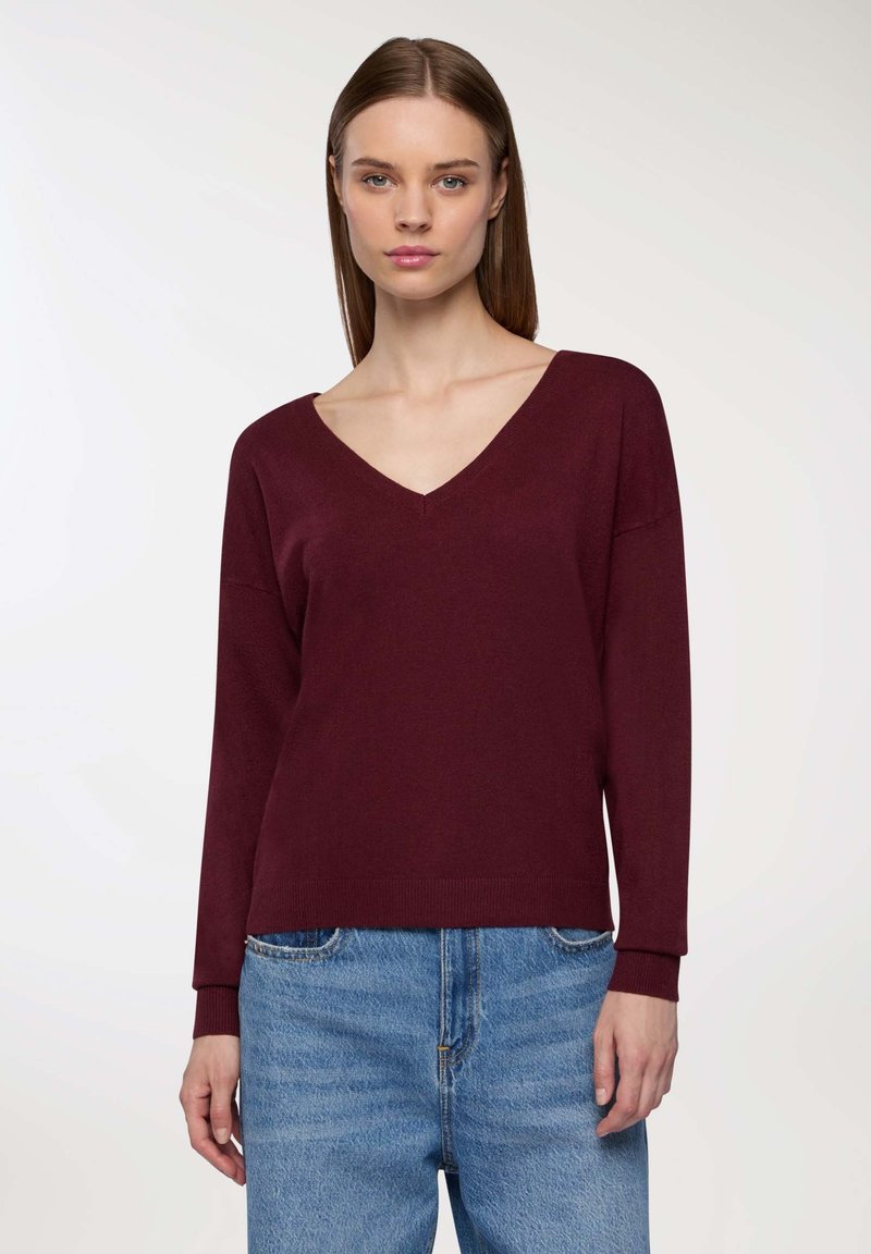 Maglione bordeaux a collo a V con maniche lunghe, tessuto morbido e polsini a costine, abbinato a jeans di denim blu chiaro. Design semplice e casual.