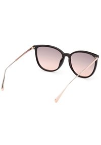 Gafas de sol estilo cat-eye en negro con lentes degradados. Finas varillas metálicas doradas con extremos curvados. Montura de plástico brillante y textura suave.