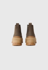 Brune lær ankle boots med gummisål og trækstropper. Designet har en kraftig hæl og minimale accenter, som skaber en strømlinet profil.