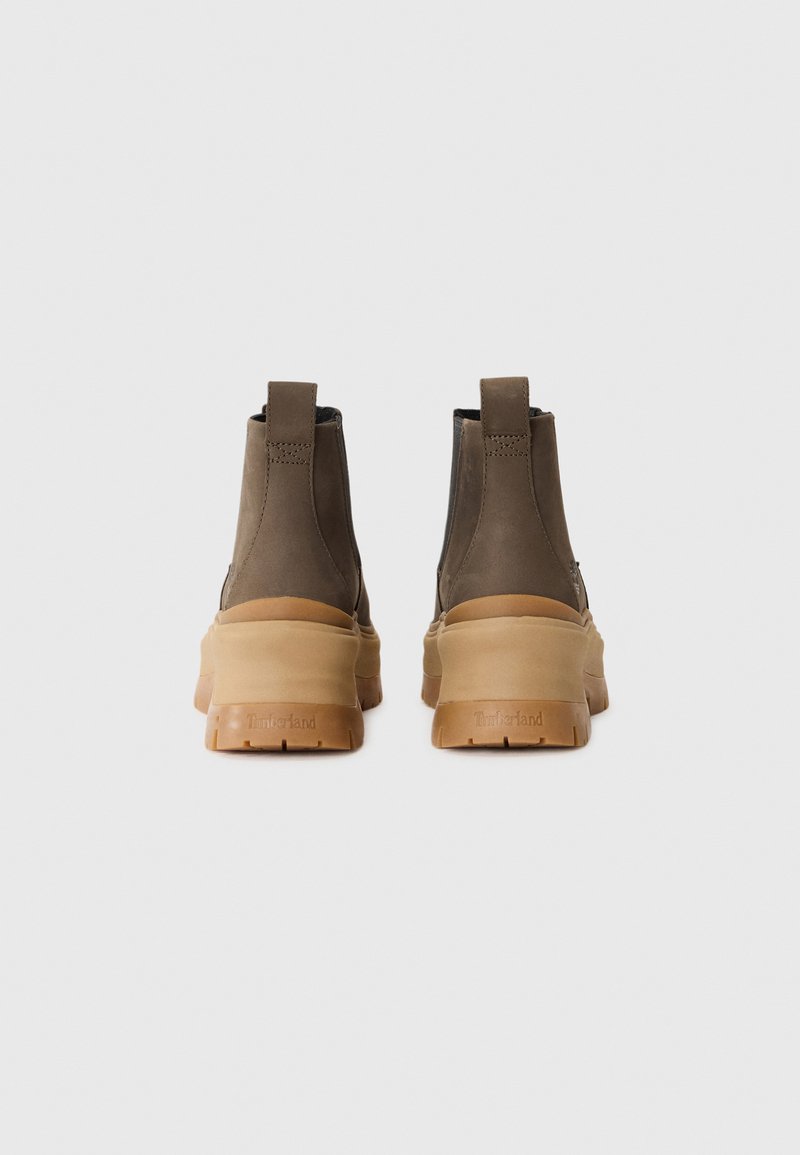 Botas de tobillo de cuero marrón con suela de goma y tiradores. El diseño presenta un tacón grueso y acentos mínimos, creando un perfil elegante.