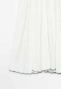 Jupe blanche à volants en tissu froissé avec un bord festonné noir le long de l'ourlet, présentée sur un fond uni.