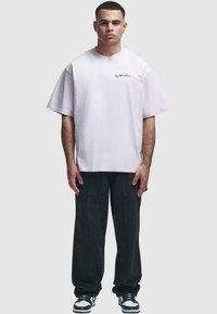 Hvit oversized bomulls t-skjorte, korte ermer, rund hals, logo på brystet, kombinert med svarte cargo-bukser og svart-hvite joggesko.