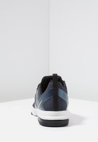 Dark blue athletic shoe with black heel pull tab, white midsole, and black outsole shown from the rear on a white surface.