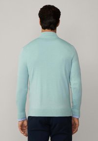 Hellblauer Langarmpullover mit strukturiertem Strick, gerippten Bündchen und geradem Saum, getragen über einem kragenlosen Hemd mit blauen Streifen.