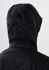 Veste à capuche noire vue de dos, avec cordon ajustable sur la capuche et texture de tissu lisse.