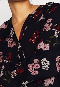 Nära bild av en person som bär en marinblå blus med röda, rosa och vita blommönster, som visar ringningen och övre ärmar.