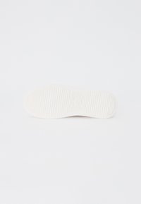 Fehér sneaker talp bordázott textúrával és kör alakú akcentussal a középpontban. Simább felület egyszerű, minimális dizájnnal.