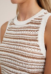 Stickad ärmlös topp med ett strukturerat mönster av växelvis vita och bruna horisontella ränder. Mjuk tygkvalitet med rund halsringning.